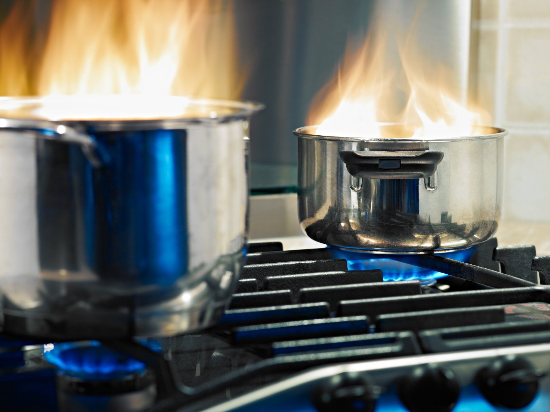 Two pots are on a stove with flames coming out of them.