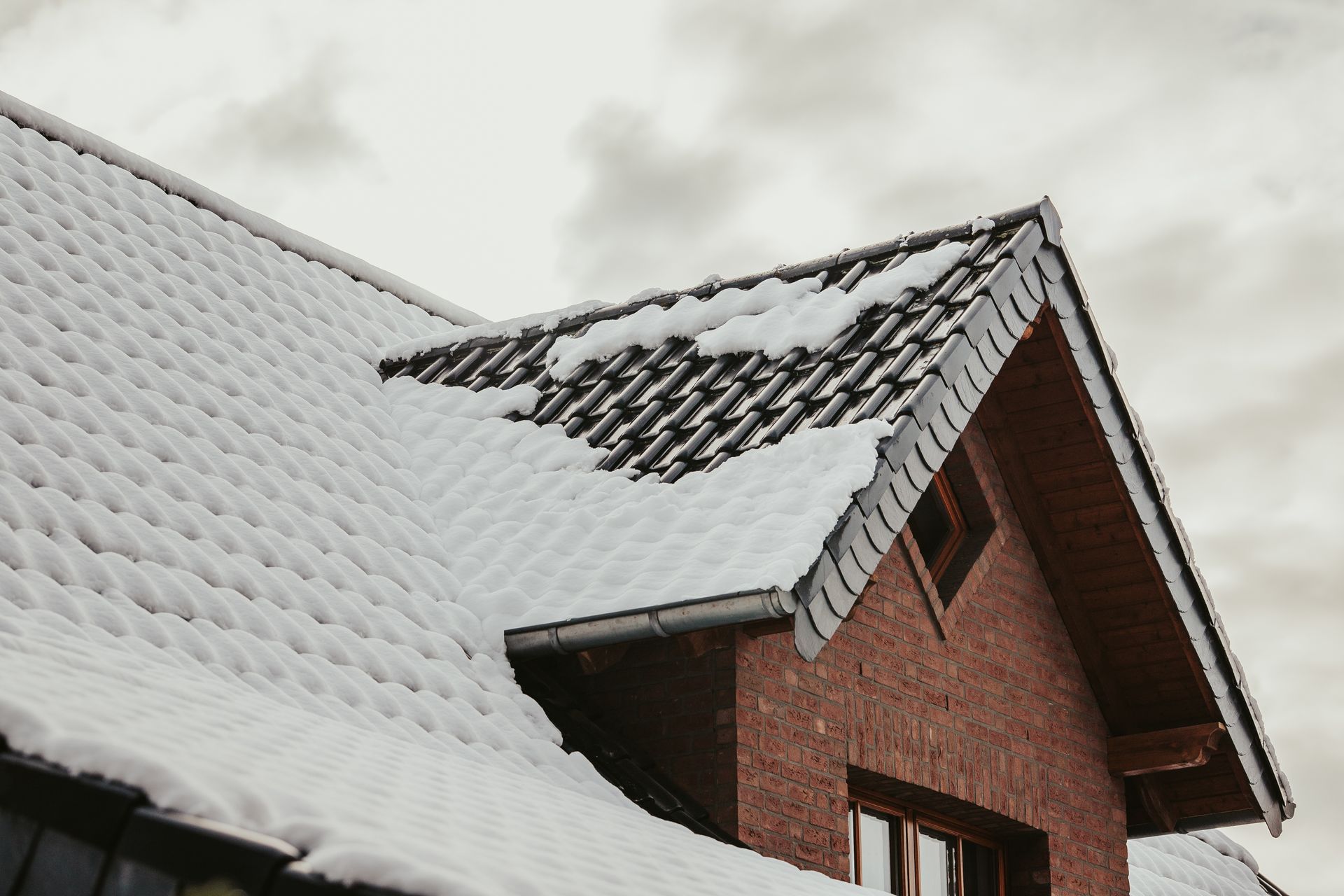 The roof of a brick house is covered in snow.