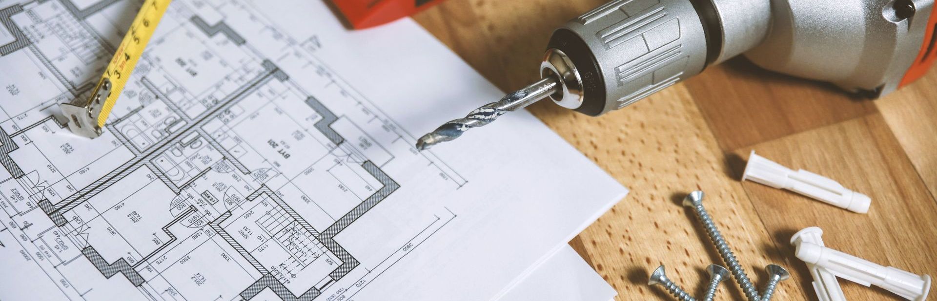 A drill is sitting on a wooden table next to a drawing of a house.