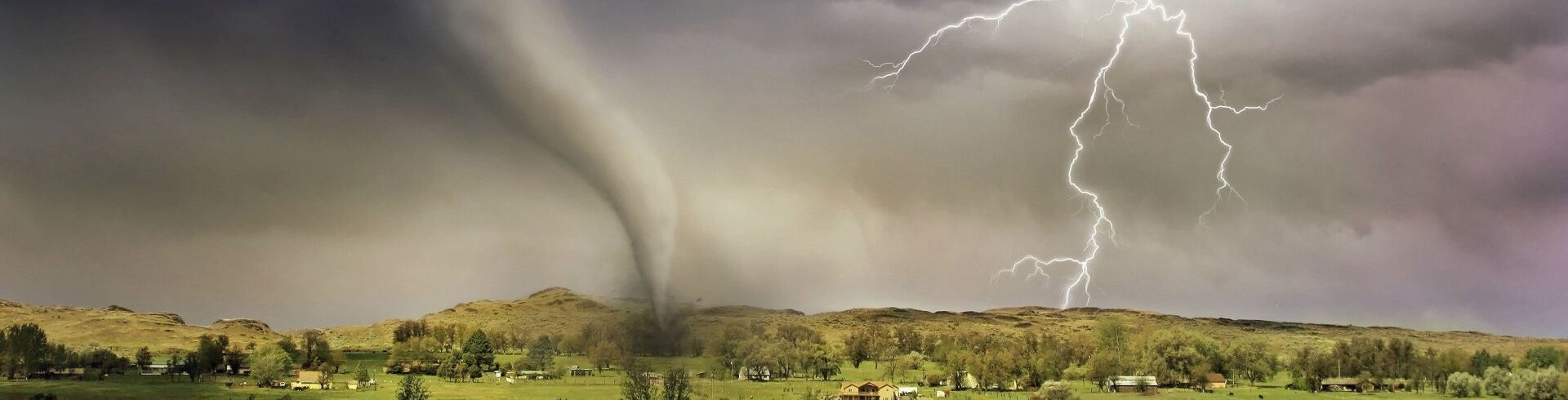 A tornado is moving through a field with lightning in the background.