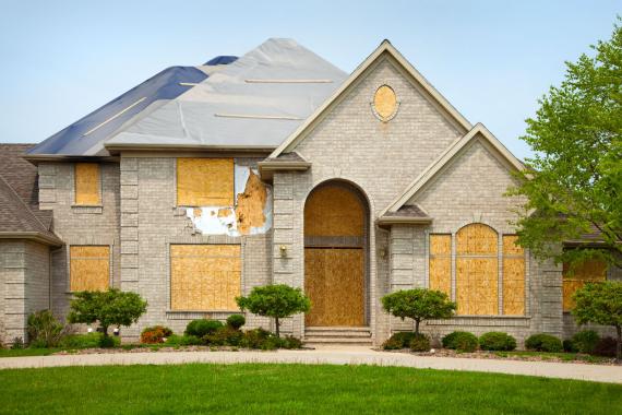 A large brick house with a roof and windows boarded up.