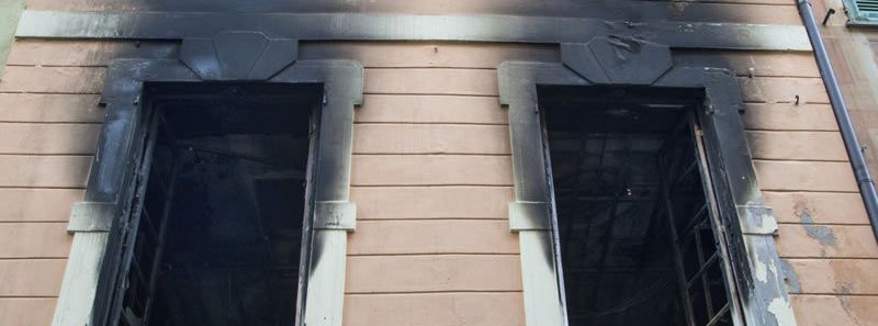 A building with two windows covered in black smoke caused by house fire.