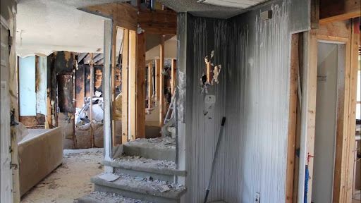The inside of a damaged house being restored with stairs and a broom.