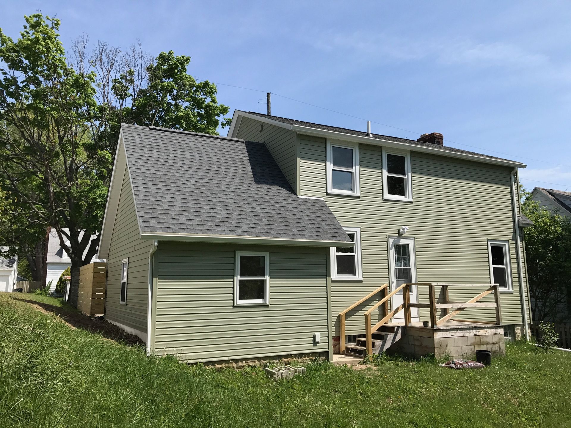 A green house with a gray roof is sitting on top of a grassy hill.