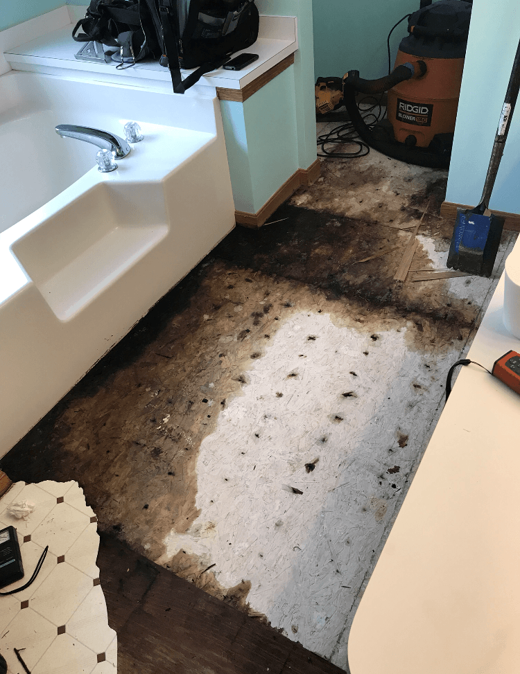 A damaged bathroom floor with a bathtub in the background..