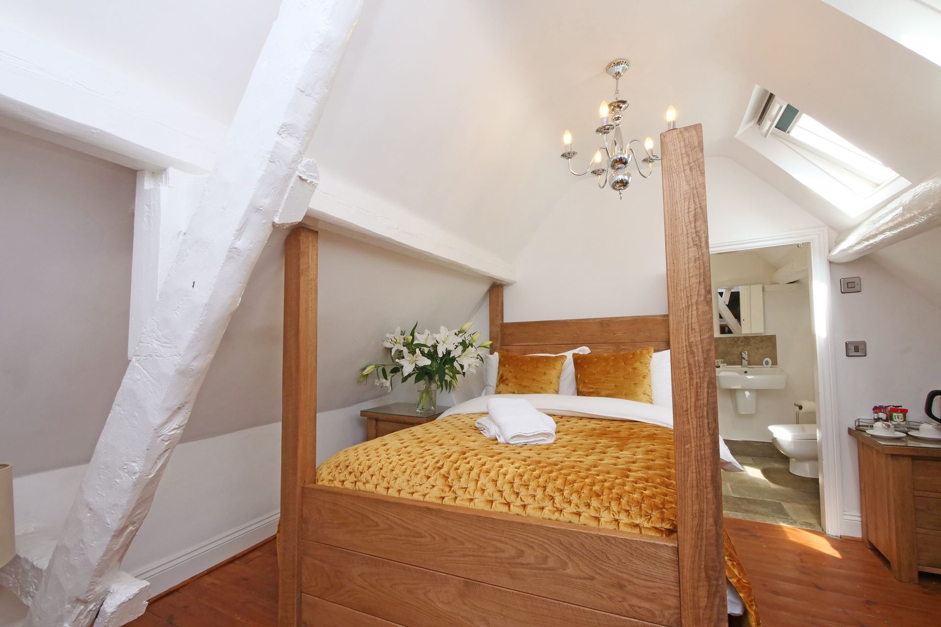 Bedroom with a wooden four-poster bed, yellow blanket and pillows, and an attached bathroom with a skylight.