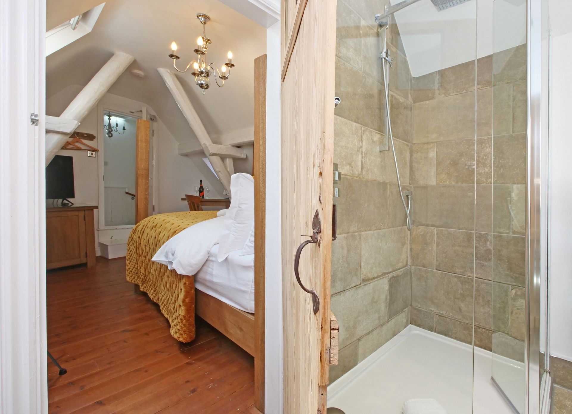 A bright bedroom with a bed and a shower visible. The shower is tiled with a glass door.