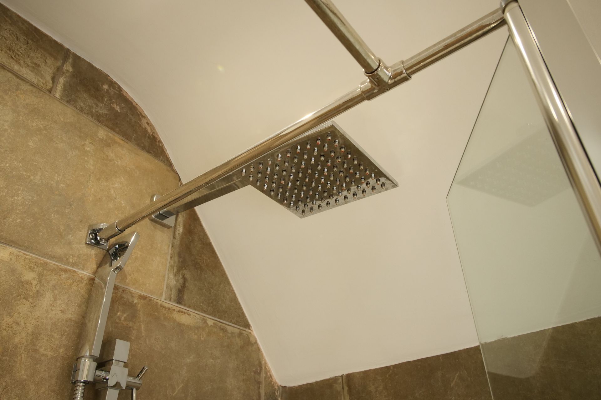 Shower head installed on an angled ceiling. The shower head is silver, and the walls are stone.
