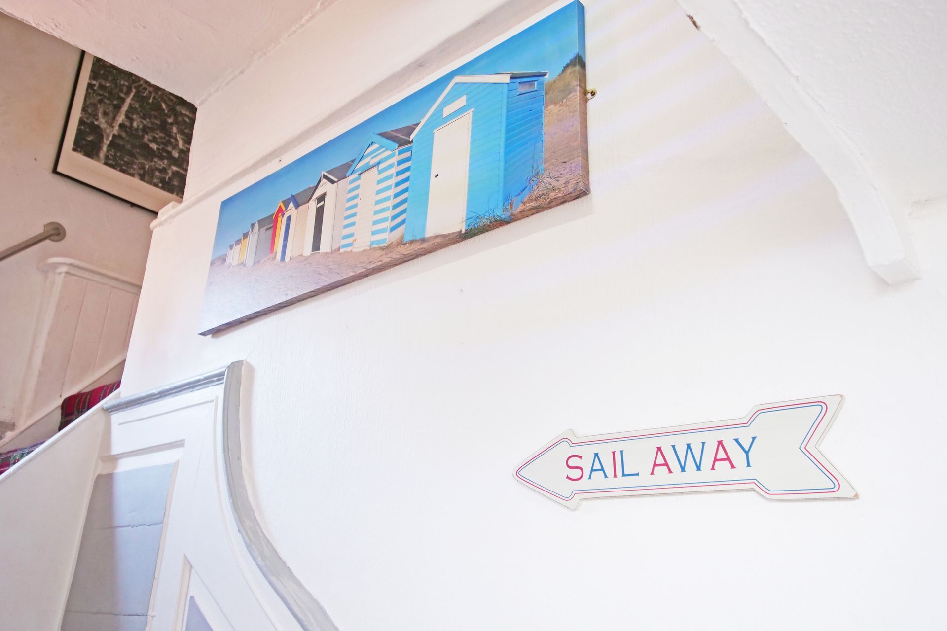 White wall with beach-themed decorations: a painting of blue beach huts, and a 