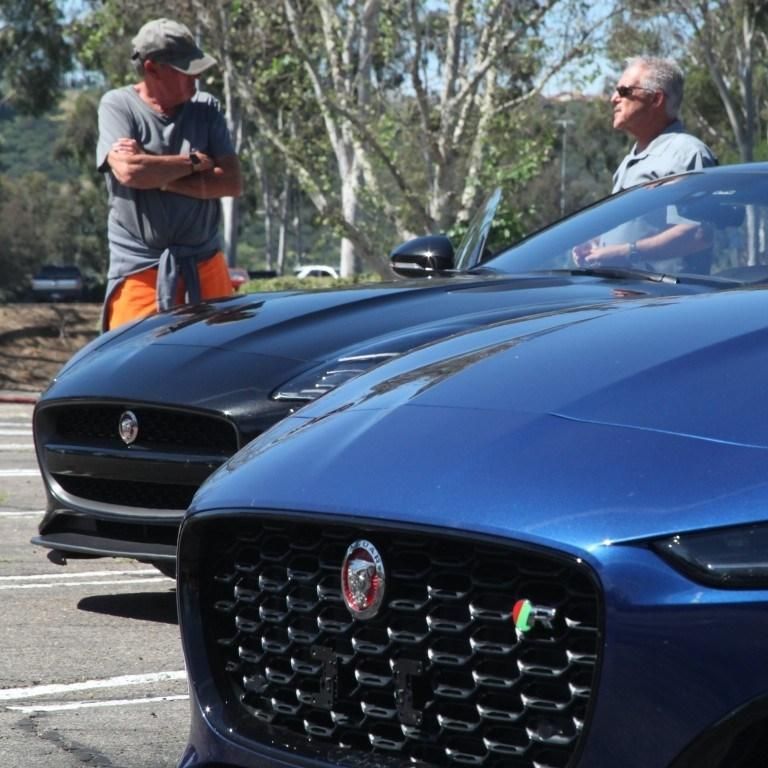 Two men talking beside a blue and a black Jaguar in a parking lot