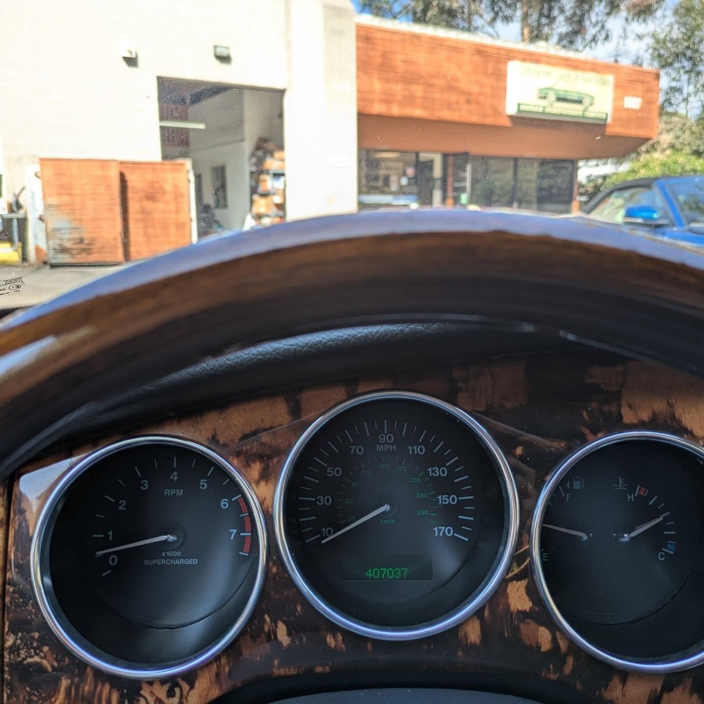 Car dashboard with three gauges and wood trim, parked in front of a storefront.