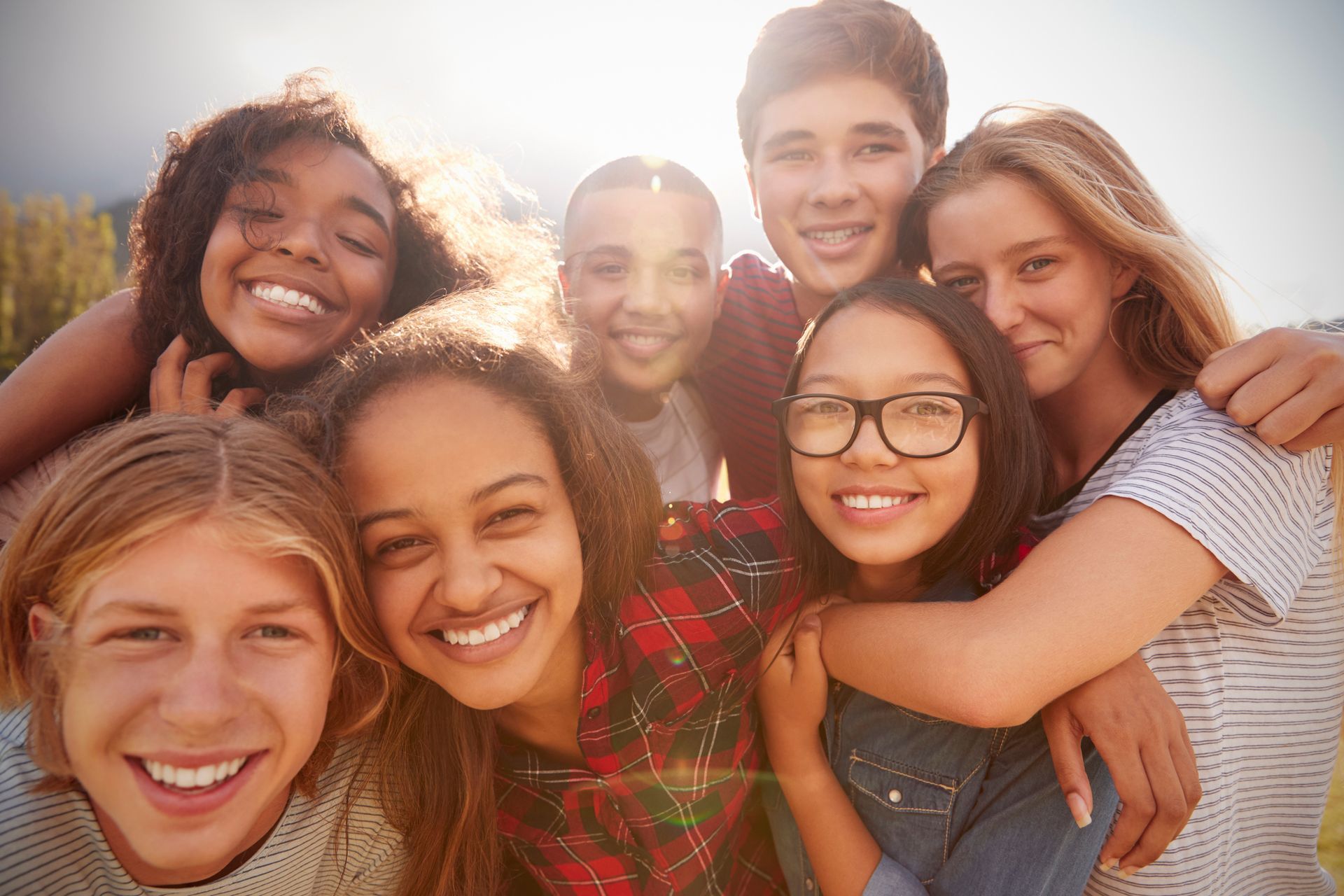 Group of smiling friends posing close together outdoors in warm sunlight.