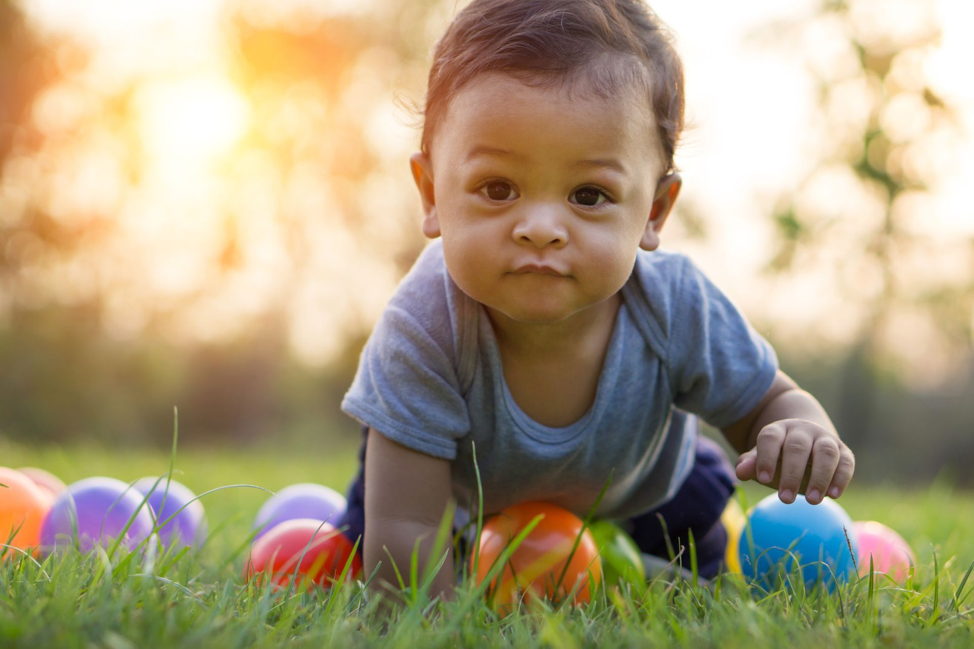 Toddler crawling on grass with colorful balls in a sunlit park