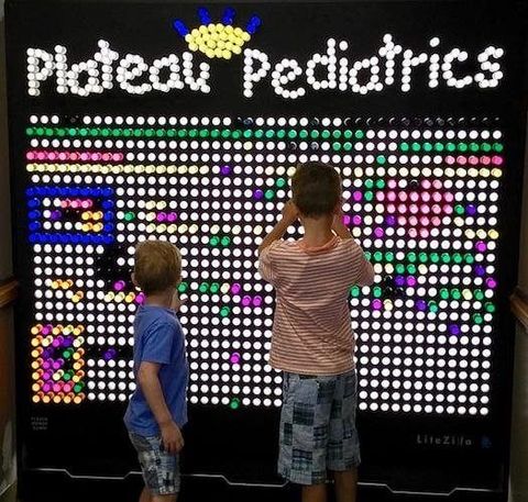 Children looking at a colorful LED sign reading “Plateau Pediatrics”