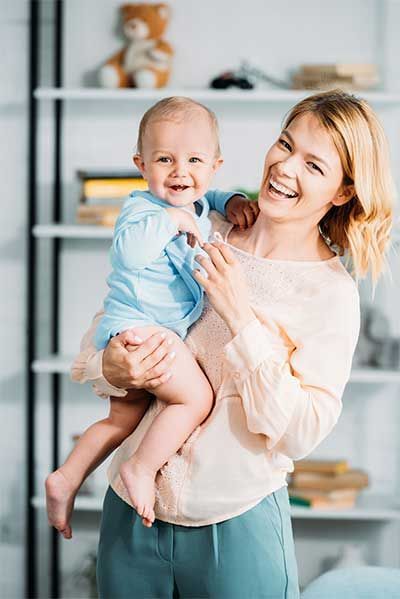 Smiling woman holding a laughing baby in a bright room with shelves in the background