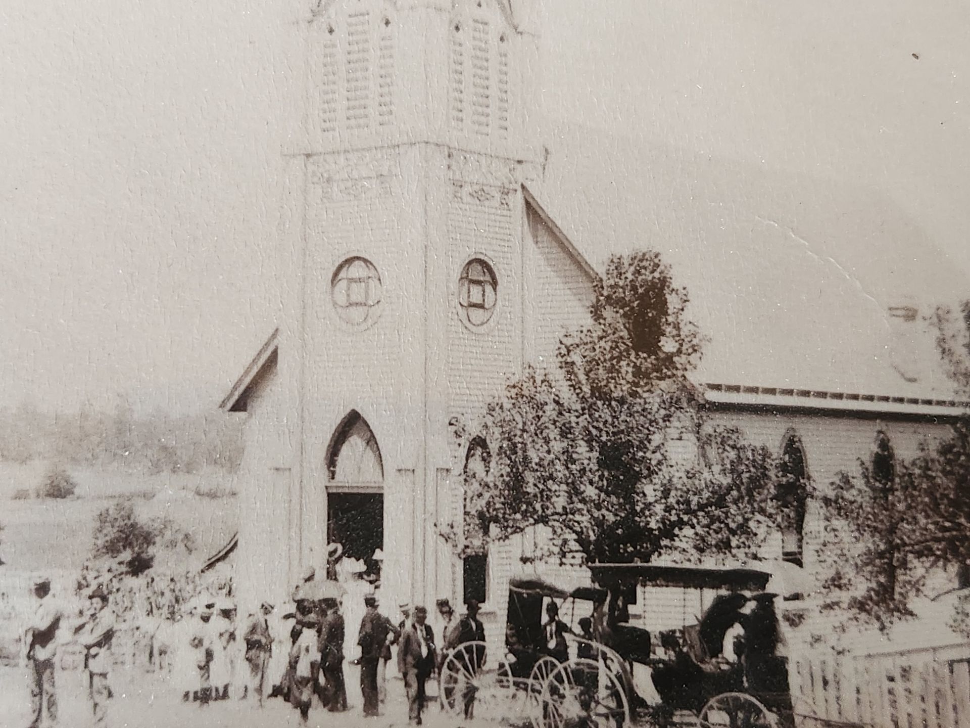 Vintage photo of people gathered outside a church with a steeple and a horse-drawn carriage.