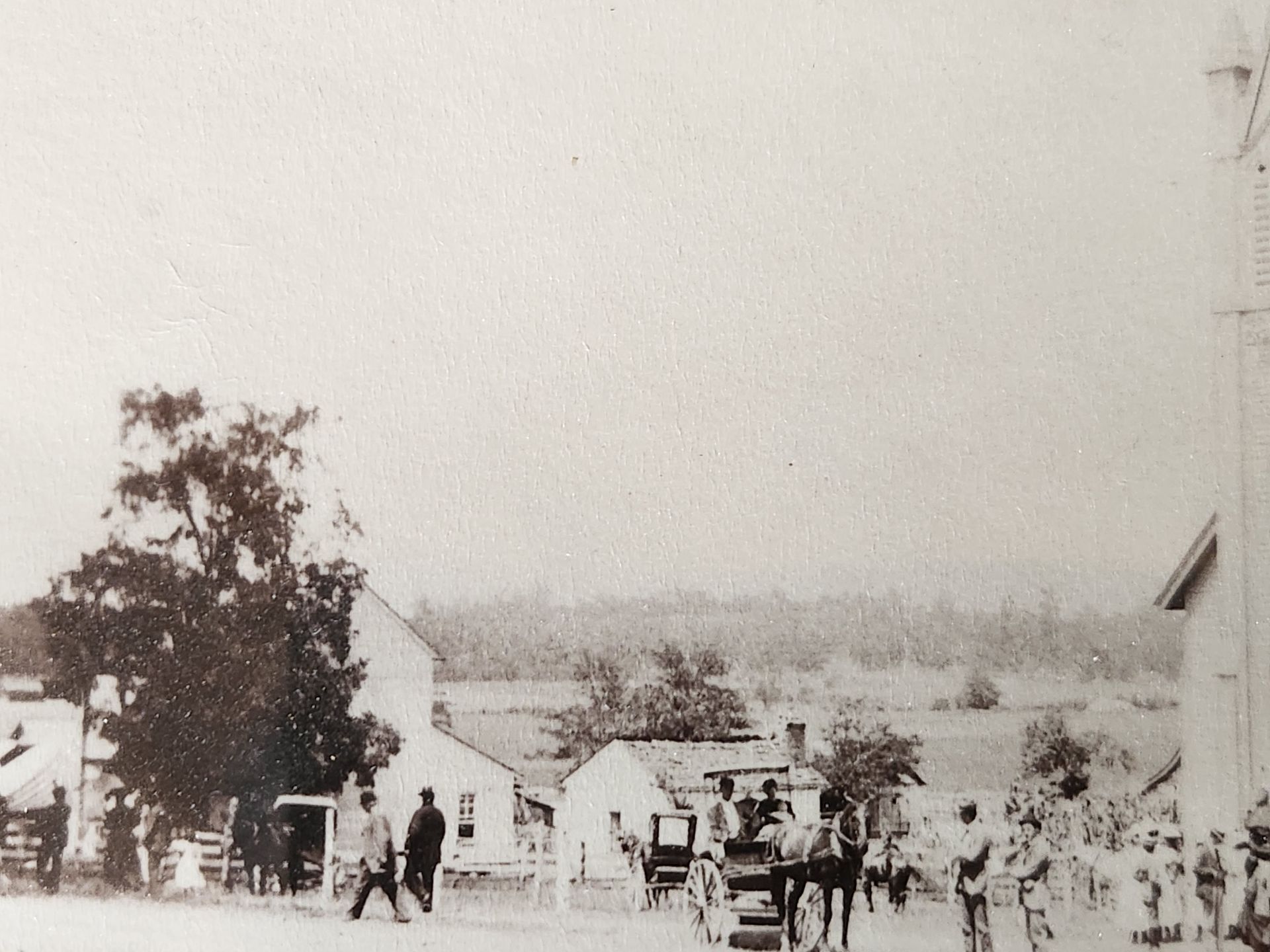 A sepia-toned photo of a small town street with people, buildings, and a horse-drawn carriage.