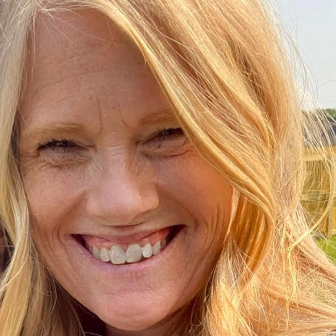 Woman with blonde hair smiles, outdoors.