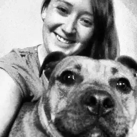 Woman smiling with her arm around a dog, both looking at the camera.