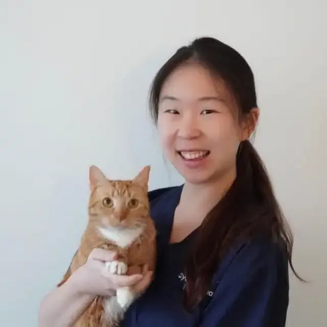 Woman holding orange cat, smiling. Both face the camera. White background.