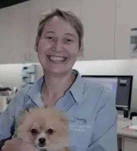 Woman in a light blue shirt holding a fluffy dog, smiling in a veterinary clinic.