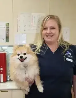 Veterinarian holding a Pomeranian dog at an office. Both smile, dog's fur is light brown.