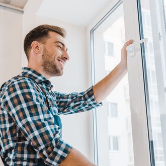 A man in a plaid shirt is opening a window.