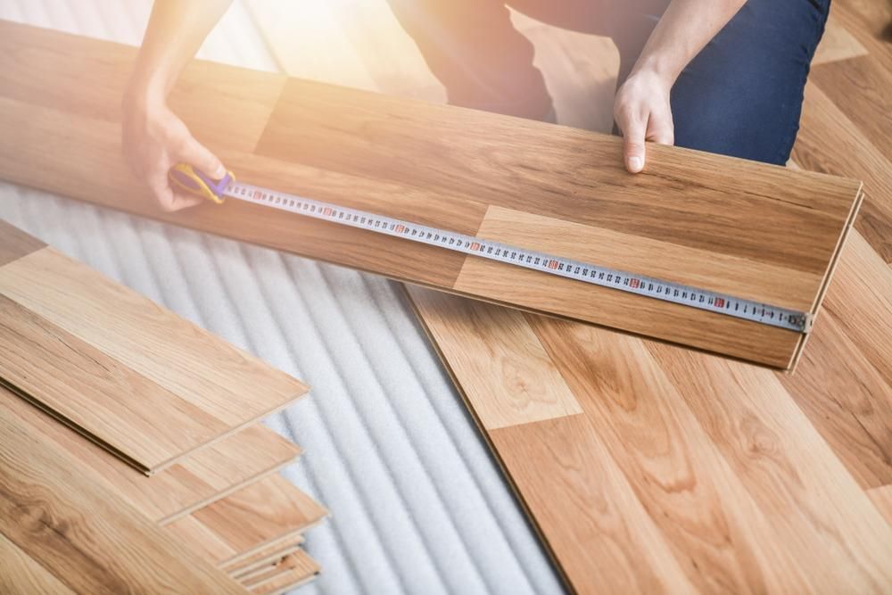 A Person Is Measuring a Wooden Floor with A Tape Measure — Nicho's Home Maintenance In Gunnedah, NSW