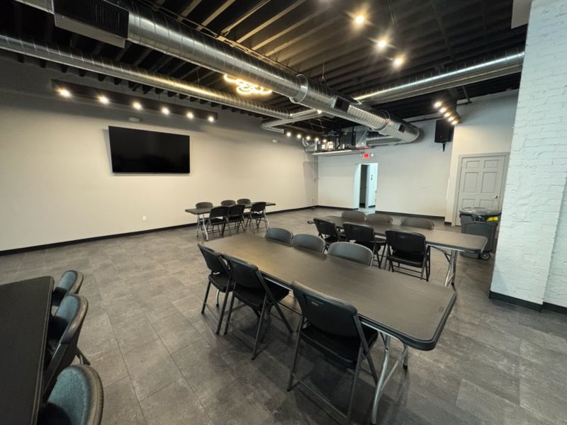 Empty modern meeting room with tables, folding chairs, a wall-mounted TV, and exposed ceiling beams