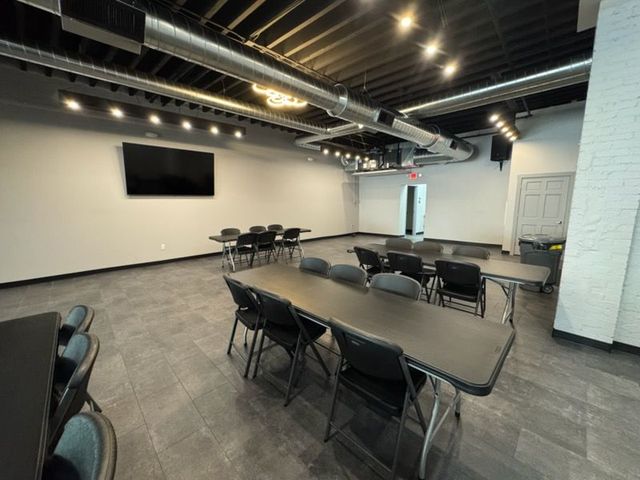 Empty modern meeting room with tables, folding chairs, a wall-mounted TV, and exposed ceiling beams