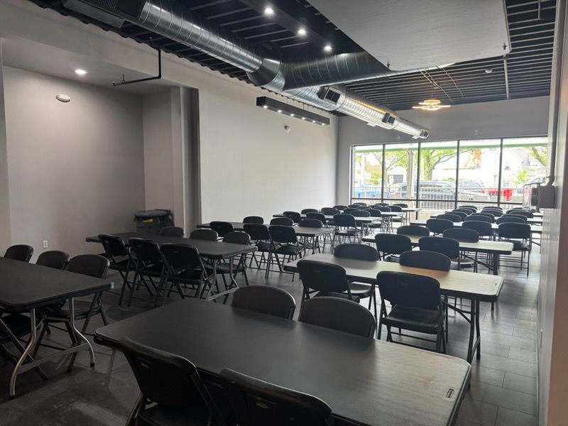Empty conference room with rows of black tables and chairs under bright ceiling lights