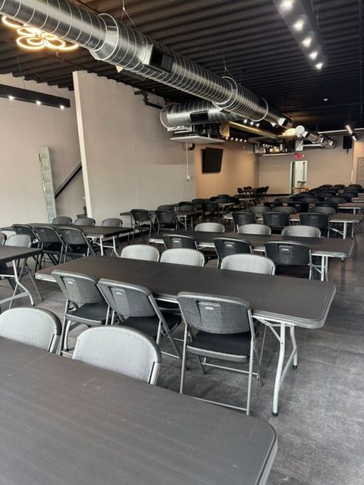 Empty dining hall with rows of black tables and gray chairs under exposed ceiling ducts