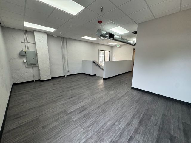 Empty office room with gray flooring, white walls, and ceiling lights