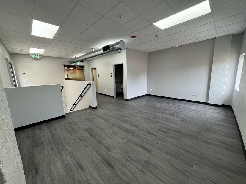Empty office space with gray carpet, white walls, fluorescent lights, and a small staircase.