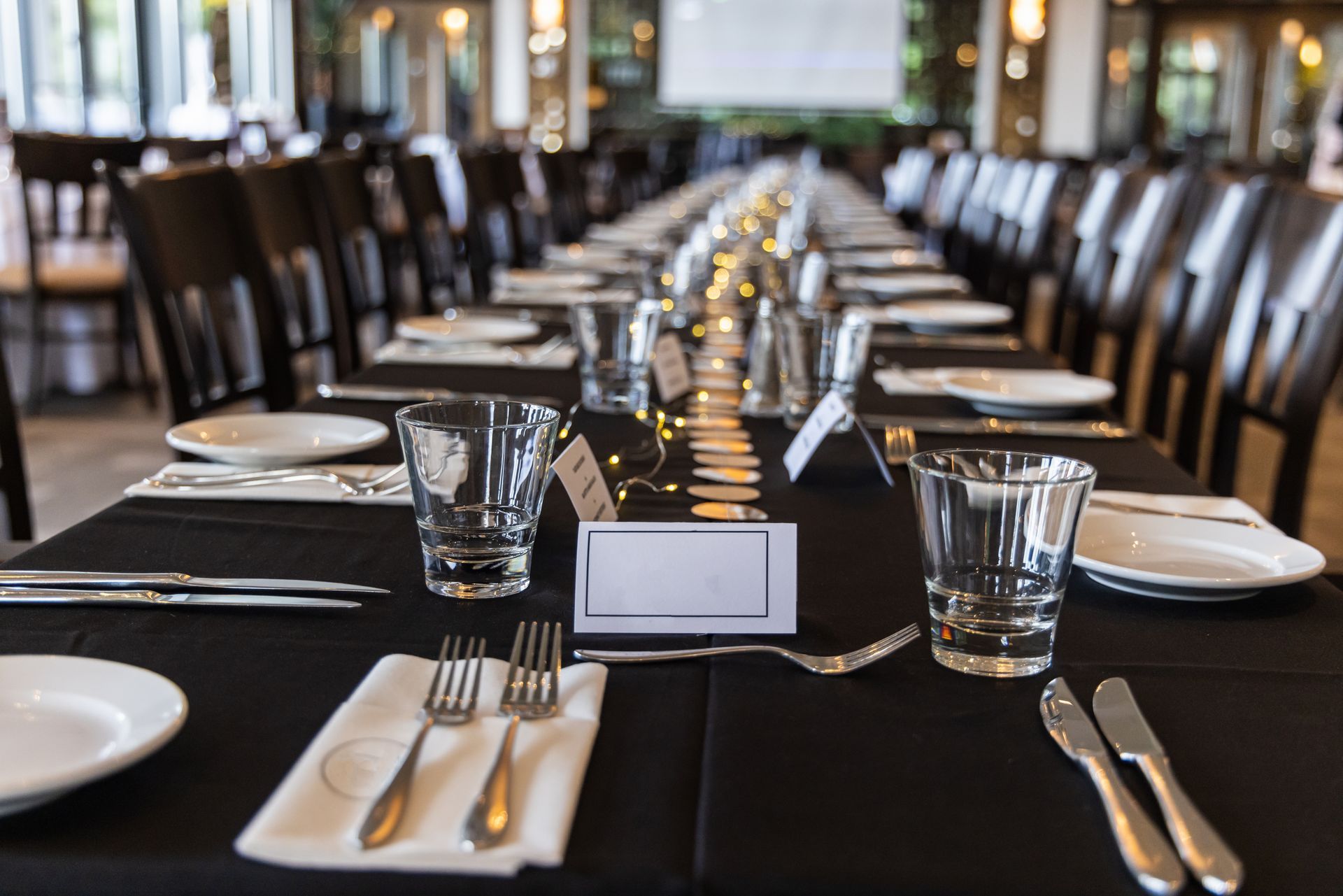 Elegant dining table set with black tablecloth, white plates, glassware, and napkins in a banquet hall
