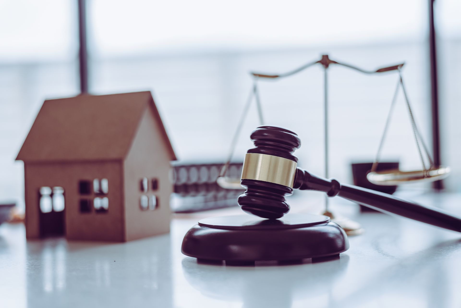 A gavel, scales of justice, and a model house on a desk, representing a property law concept.