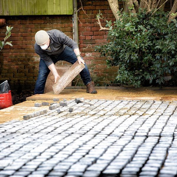 A man is laying bricks on a driveway. A man is laying bricks on a driveway.