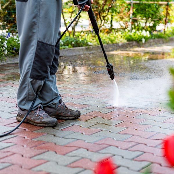 A man is using a high pressure washer to clean a brick walkway. A man is using a high pressure washer to clean a brick walkway.