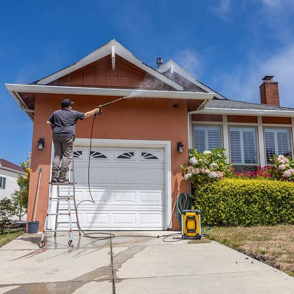 A man is standing on a ladder cleaning a house with a high pressure washer. A man is standing on a ladder cleaning a house with a high pressure washer.