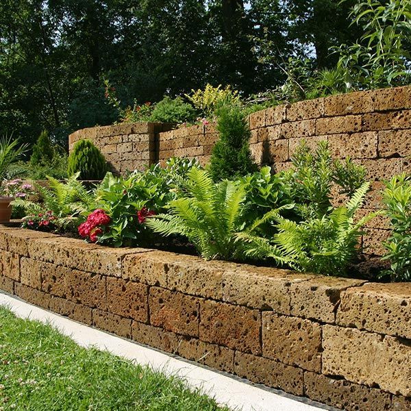 A stone wall surrounds a garden with flowers and ferns A stone wall surrounds a garden with flowers and ferns