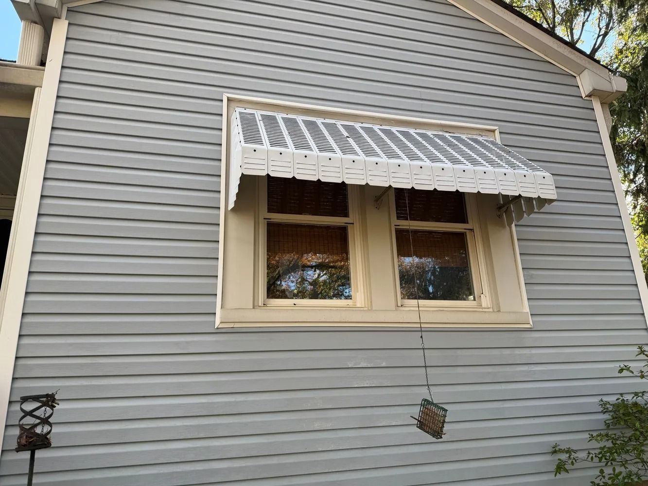 A light gray siding wall with a window featuring a white and gray striped metal awning.