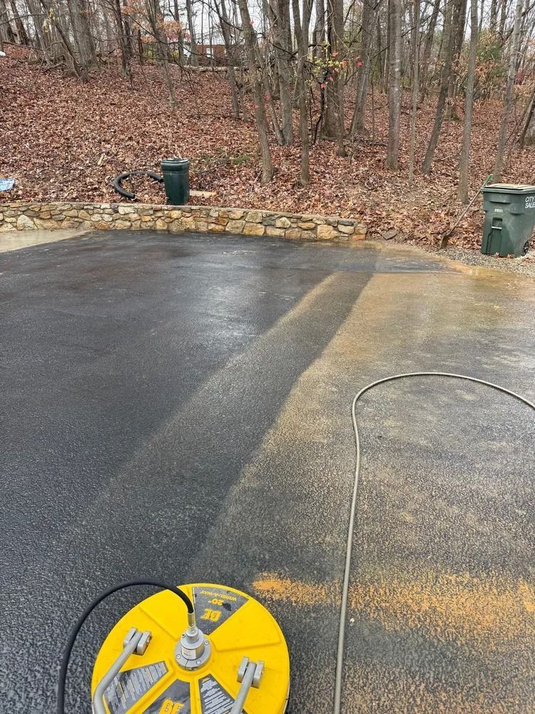 A yellow surface cleaner on a driveway, showing a clear contrast between the cleaned dark section and the dirty area.