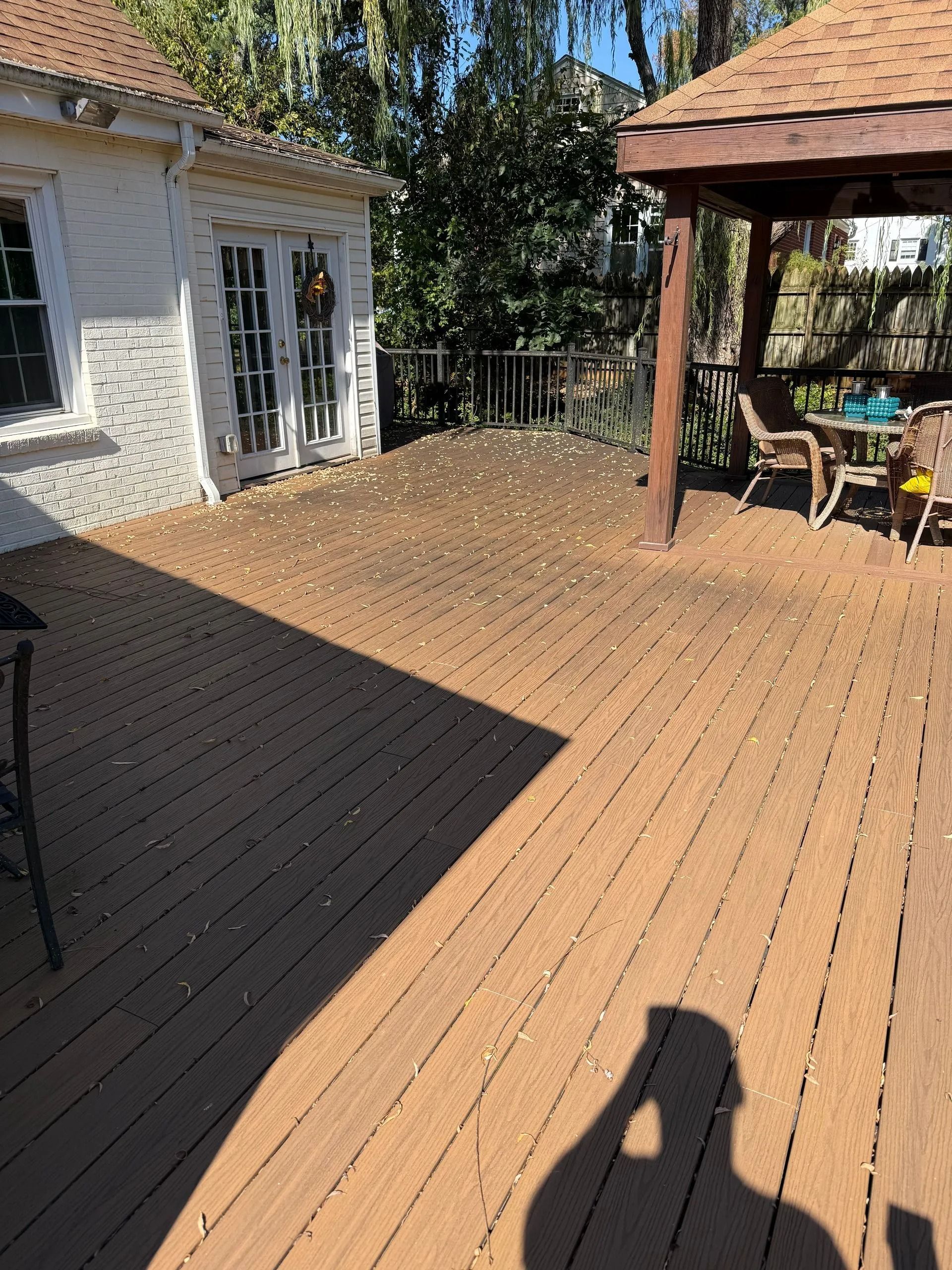 A wooden backyard deck with a gazebo, outdoor furniture, and scattered leaves, viewed from a slightly elevated position.