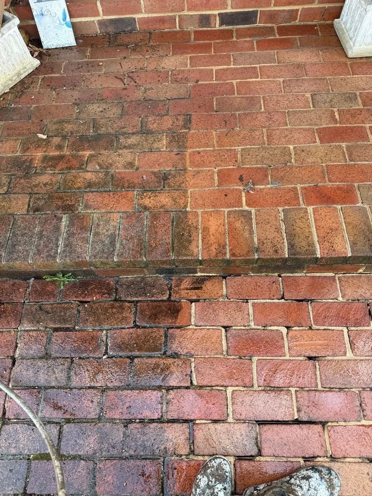 A split-view showing red brick flooring, with the left side covered in dirt and the right side recently pressure-washed.