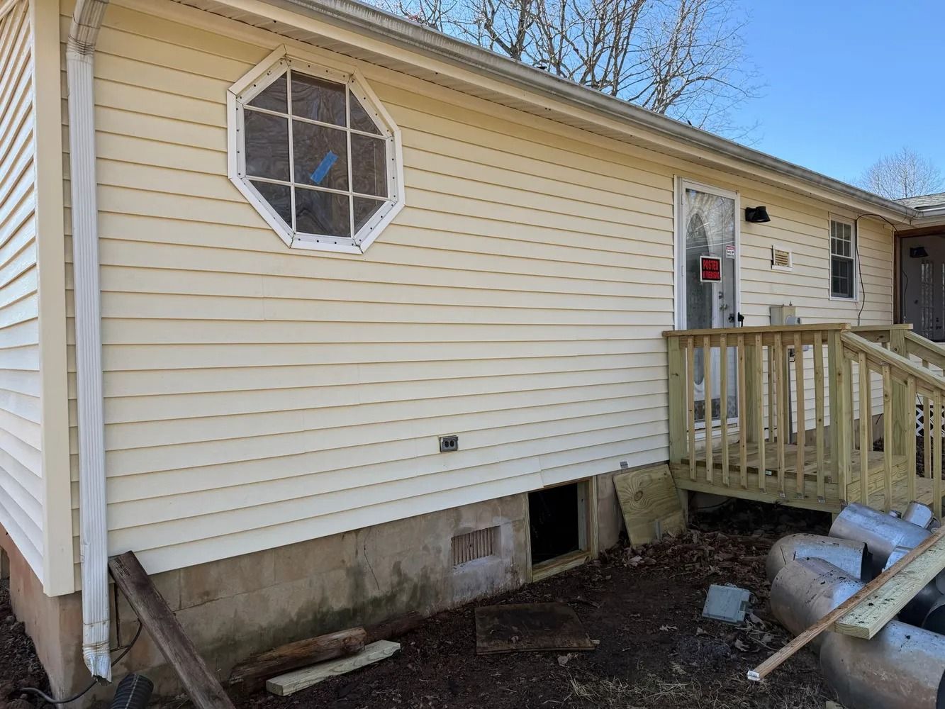 Cream-colored house exterior featuring an octagonal window, a wooden porch, and a concrete foundation with a crawl space.