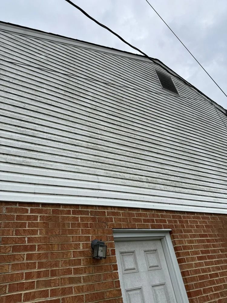 A two-story building exterior showing a brick ground floor, a white siding upper level, and a doorway.