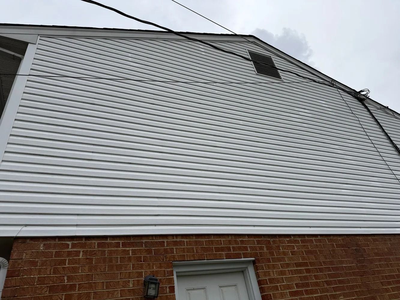 A multi-story building exterior with a white vinyl-sided upper level above a red brick lower level and a small attic vent.