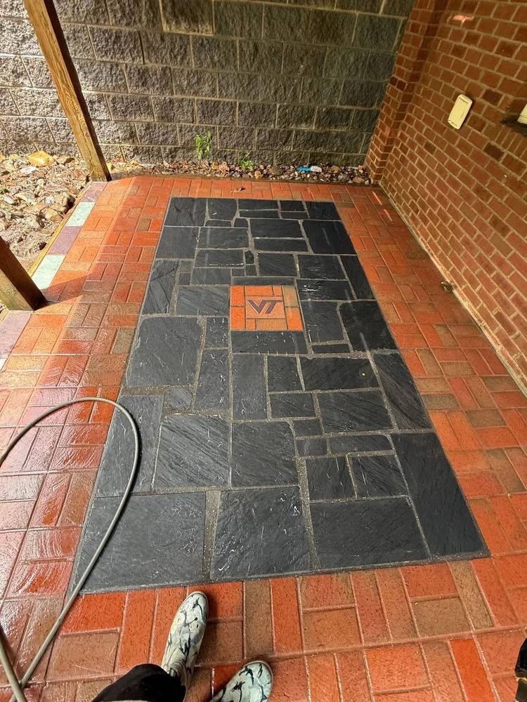 Rectangular patio with dark stone pavers, a central Virginia Tech logo brick, and red brick border.