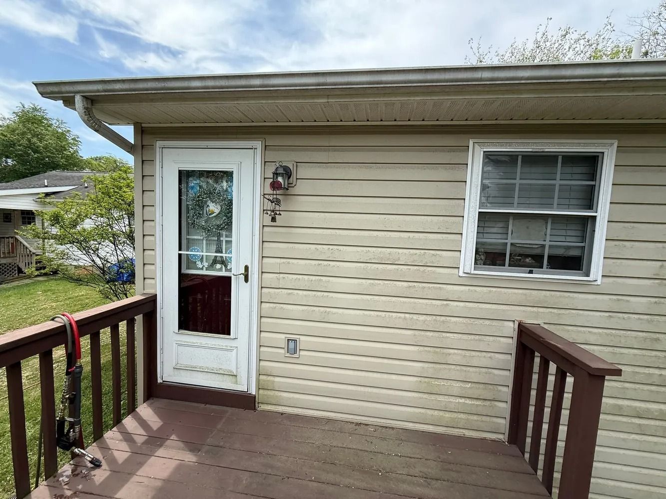 A wooden deck leads to a door and a window on the light-colored, vinyl-sided wall of a house.