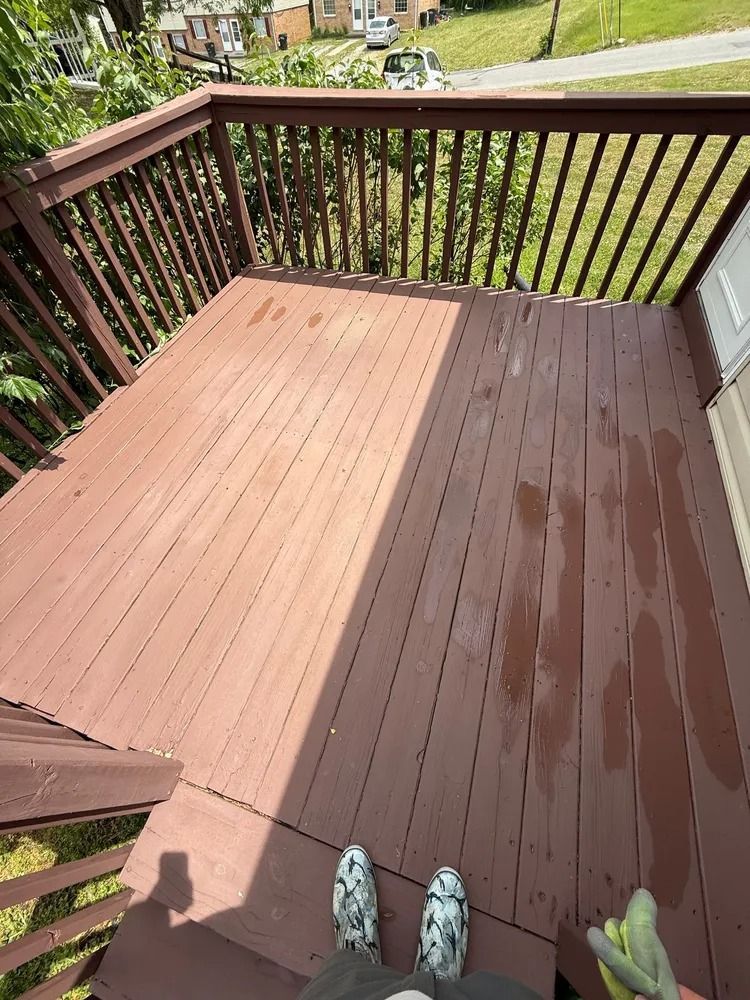 A person stands on a wooden deck, showing a contrast between the dry, weathered left side and the freshly stained right.